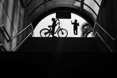 Low angle view of silhouette boy with bicycle by brother on steps