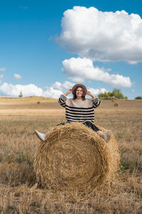 Man with hay bales on field against sky