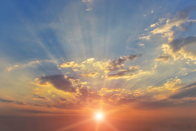 Low angle view of sunlight streaming through clouds during sunset