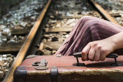 Midsection of woman holding suitcase while sitting on railroad track