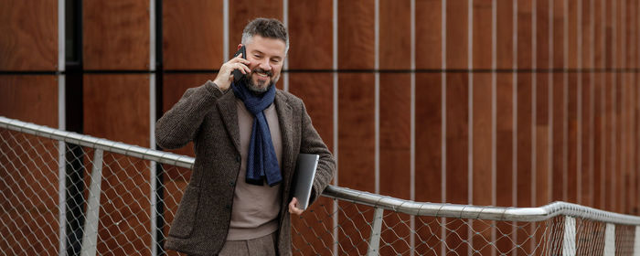 Young man using mobile phone while standing on railing