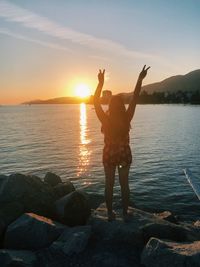 Man standing on rock against sea during sunset