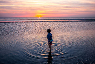 Rear view of boy standing at beach during sunset