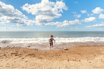 Full length of boy running on beach against sky