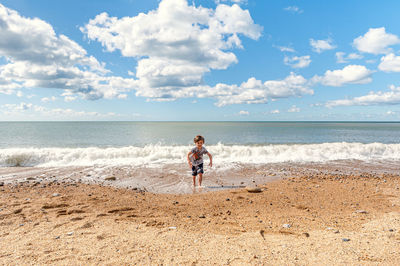 Full length of boy running on beach against sky