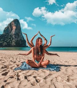 Young woman sitting on chair at beach against sky