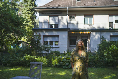 Mature woman standing with eyes closed in front yard