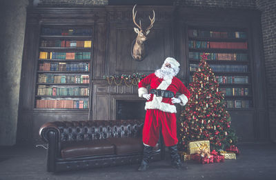 Man wearing santa claus costume standing by christmas tree at home