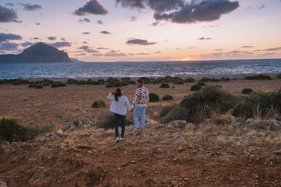 People standing on beach against sky during sunset