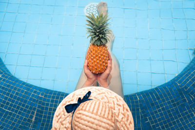 High angle view of woman holding pineapple while sitting in swimming pool
