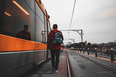 Rear view of young man with backpack standing on street against sky