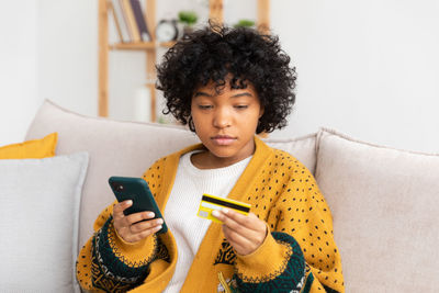 Young woman using mobile phone while sitting on sofa at home