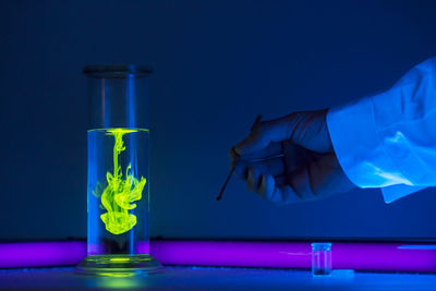 Cropped hand of scientist by container with liquid on table
