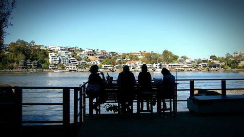 Rear view of people sitting on table by sea against clear sky