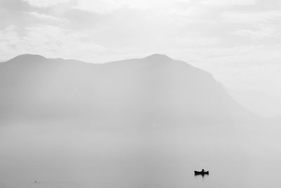 Silhouette boat moored on lake by mountain during foggy weather