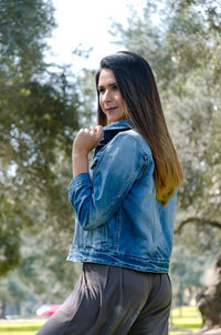 Smiling young woman looking away while standing against trees