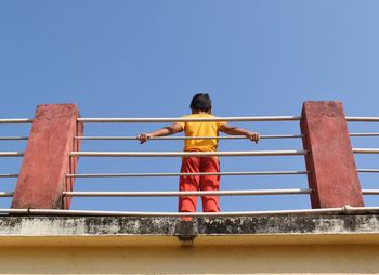 Rear view of man on railing against clear blue sky