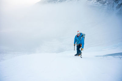 A male alpine climber ascends a steep section of snow with clouds