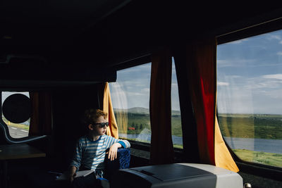 Boy wearing sunglasses looking through window while sitting in motor home