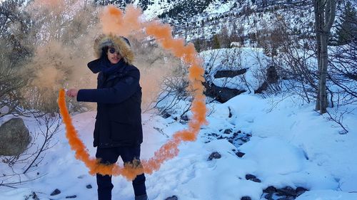 Man holding distress flare while standing on snow covered field