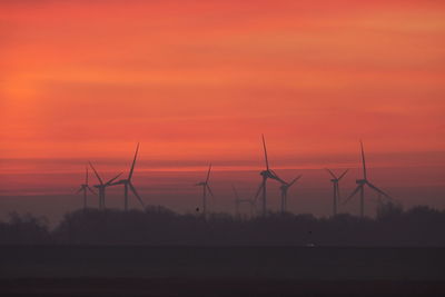 Silhouette of wind turbines on field against orange sky