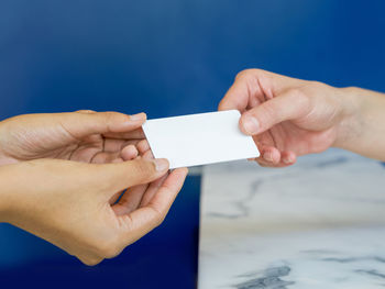 Close-up of hand holding paper against blue wall