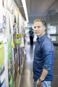 Portrait of young student standing in front of bulletin board at college