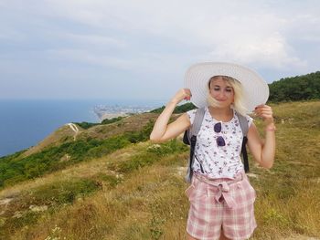 Full length of smiling woman standing on rock by sea against sky