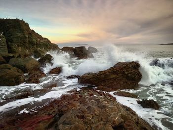 Waves splashing on rocks at shore against sky