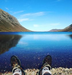 Low section of man relaxing on lake against blue sky