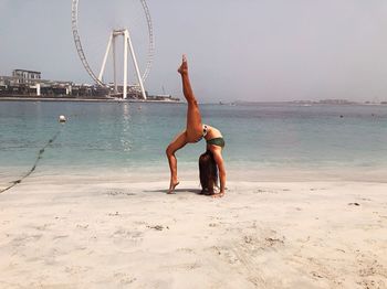 Full length of woman balancing at beach against clear sky