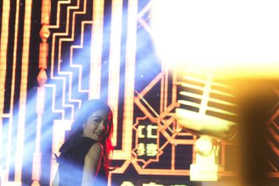 Close-up of woman in illuminated building against sky at night