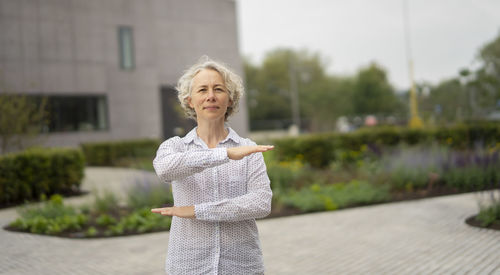 Portrait of mature woman gesturing while standing on footpath