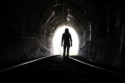 Rear view of woman standing on railroad track in tunnel