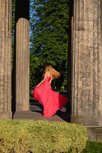 Full length of young woman in pink evening gown dancing at colonnade