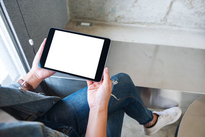 Midsection of woman using digital tablet by window