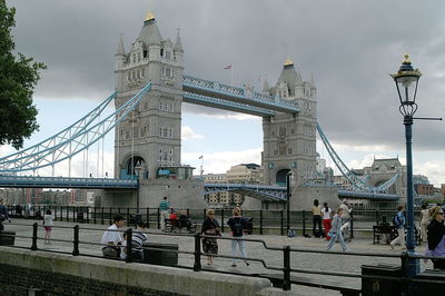 Tourists on bridge against cloudy sky