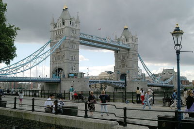 People walking by tower bridge against cloudy sky