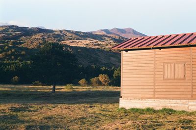 House on field by mountains against clear sky