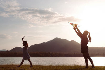 Rear view of woman with arms raised standing against lake during sunset