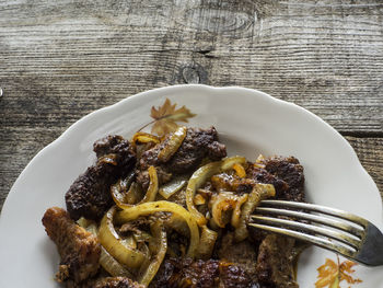 Close-up of fried pork and onion in plate on wooden table