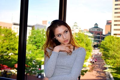 Young woman looking away while standing by window in city