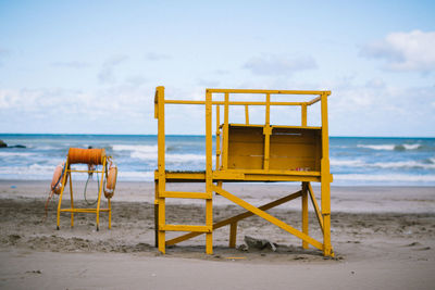 Lifeguard chair on sand at beach against sky
