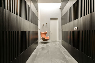 Perspective view of hallway interior with gray striped walls and brown chair placed near entry door