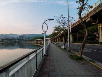 Footpath by canal in city against sky