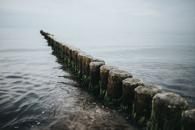 Close-up of weathered wooden posts in sea against sky