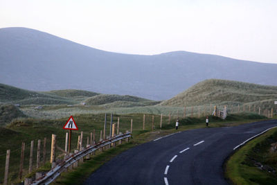 Empty road leading towards mountains against clear sky