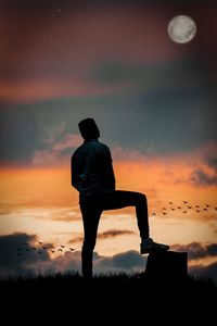 Rear view of silhouette man standing on field against sky during sunset