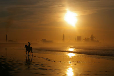 Silhouette man walking on beach against sky during sunset