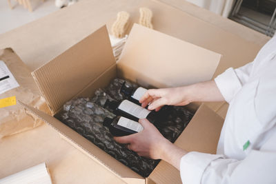 High angle view of female owner unpacking cardboard box containing bottles in workshop